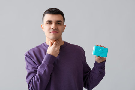 Young man with thyroid gland problem and pill box on light background