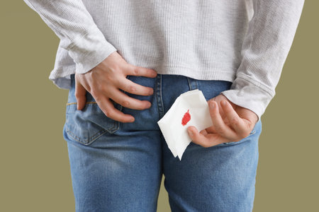 Young man with bloody toilet paper on green background, back view. Hemorrhoids concept