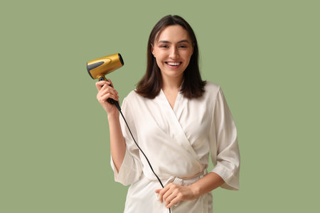 Beautiful young woman with hair dryer on green backgroundの写真素材