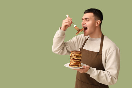 Young man eating tasty homemade pancakes on green backgroundの写真素材