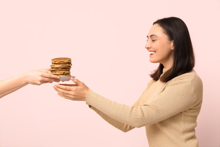 Hands giving young woman stack of tasty pancakes on pink backgroundの写真素材
