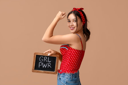 Beautiful young Asian pin-up woman holding chalkboard with text GIRL POWER and showing her muscles on brown backgroundの写真素材