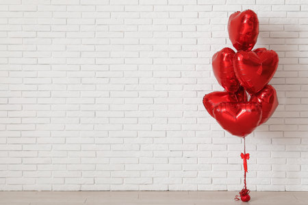 Red heart-shaped balloons near white brick wall. Valentine's Day celebrationの写真素材