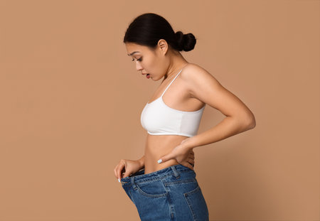 Young woman in loose jeans after weight loss on beige backgroundの写真素材