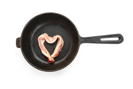 Frying pan with heart made of tasty bacon on white backgroundの写真素材