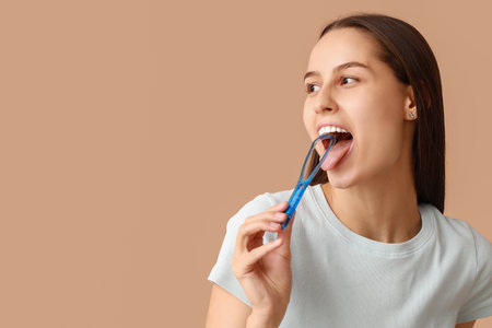 Beautiful young woman with tongue scraper on brown backgroundの写真素材