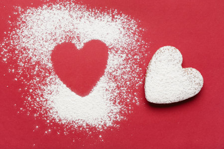 Heart made of sugar powder and sweet cookies on red background. Valentine's day celebrationの写真素材