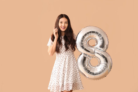Beautiful young Asian woman with silver air balloon in shape of figure 8 on brown background. International Women's Dayの写真素材
