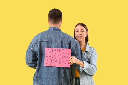 Lovely couple holding greeting card with text HAPPY VALENTINE'S DAY on yellow backgroundの写真素材