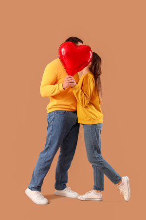 Lovely couple covering faces with heart-shaped balloon on beige background. Valentine's Day celebrationの写真素材