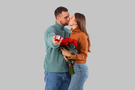 Lovely couple with bouquet of roses and wedding ring on gray background. Valentine's Day celebration