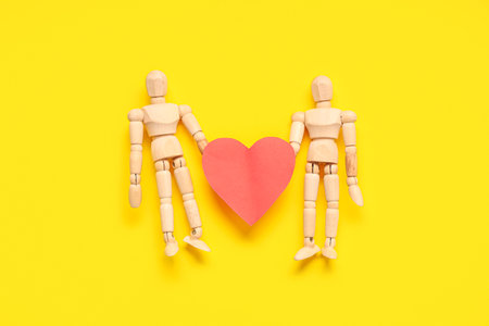 Wooden mannequins with paper heart on yellow background. Valentine's day celebrationの写真素材