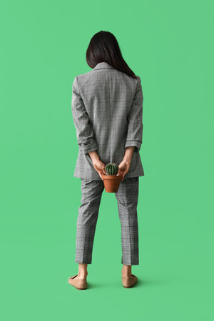 Young businesswoman with hemorrhoids and cactus on green background, back viewの写真素材