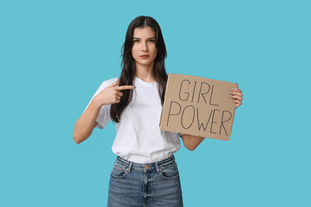 Young woman pointing at cardboard with text GIRL POWER on blue background. Feminism conceptの写真素材