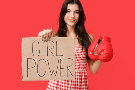 Young woman with sign GIRL POWER and boxing gloves on red background. Feminism conceptの写真素材