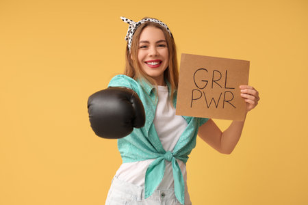 Happy young pin-up woman in boxing glove holding card with text GIRL POWER on yellow backgroundの写真素材