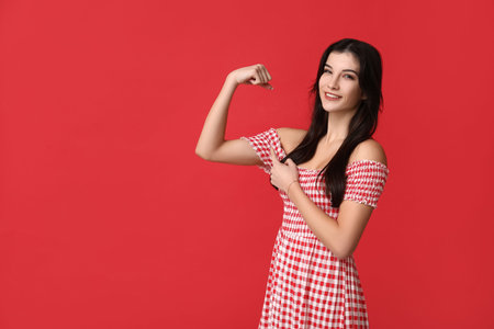 Young woman flexing muscles on red background. Feminism conceptの写真素材
