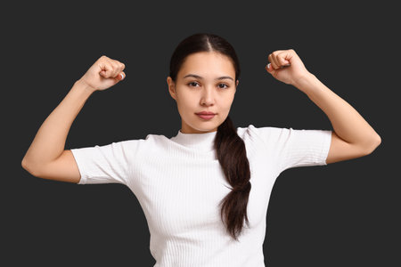 Young woman flexing muscles on black background. Feminism conceptの写真素材
