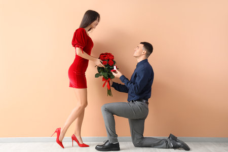 Young man with bouquet of roses proposing to his girlfriend on beige background. Valentine's Day celebrationの写真素材