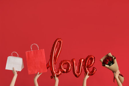 Women with shopping bags, word LOVE made of balloons and roses on red background. Valentine's Day celebrationの写真素材