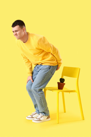 Young man with hemorrhoids and cactus on chair against yellow backgroundの写真素材