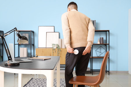 Young businessman with a sad smile in office, back view. Hemorrhoids conceptの写真素材