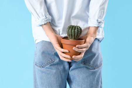 Young man with hemorrhoids and cactus on blue background, back viewの写真素材