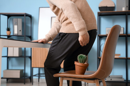 Young businessman with hemorrhoids and cactus on chair in officeの写真素材