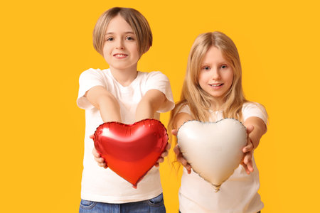 Little children with heart-shaped balloons on yellow background. Valentine's Day celebrationの写真素材