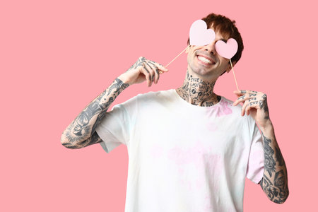 Funny young man with paper hearts on pink backgroundの写真素材