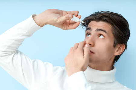 Young man using eye drops on blue background, closeup. Glaucoma awareness monthの写真素材