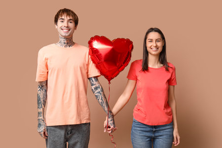Young couple with heart-shaped air balloon holding hands on beige backgroundの写真素材