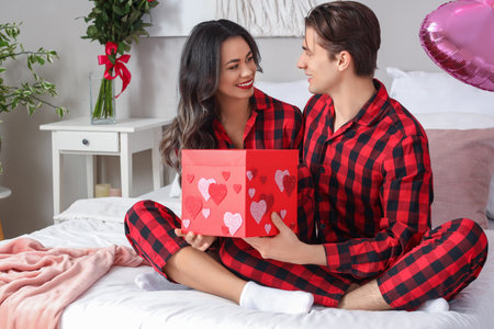 Young couple with gift box in bedroom on Valentine's Dayの写真素材