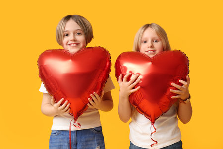 Little children with heart-shaped balloons on yellow background. Valentine's Day celebrationの写真素材