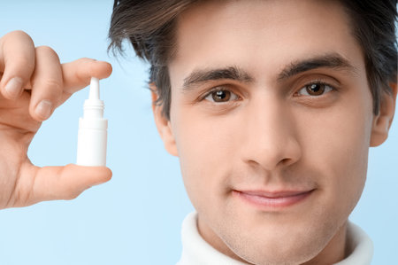 Young man with eye drops on blue background, closeup. Glaucoma awareness monthの写真素材