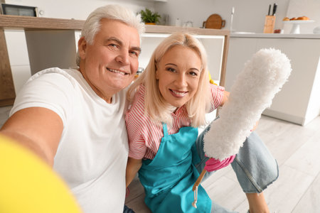 Mature couple taking selfie after cleaning in kitchenの写真素材