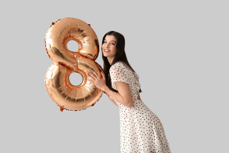 Beautiful young woman with golden air balloon in shape of figure 8 on gray background. International...
