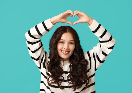 Happy young Asian woman showing heart gesture on blue background. Valentine's Day celebrationの写真素材