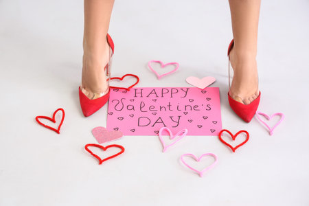 Female legs with gift card for Valentine's day and decorative hearts on gray background