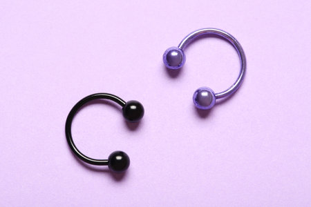 Colorful circular barbells for piercing on lilac background