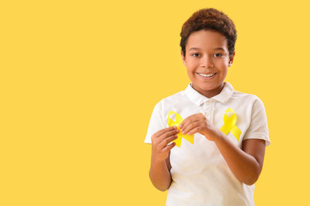 Cute little African-American boy with yellow ribbons on color background. Childhood cancer awareness conceptの写真素材