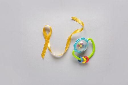 Golden ribbon with baby rattle on white background. Childhood cancer awareness concept