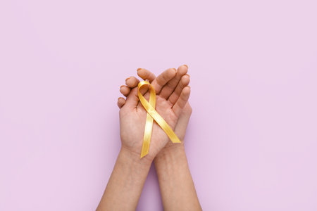 Hands with golden ribbon on lilac background. Childhood cancer awareness conceptの写真素材