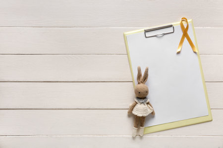 Golden ribbon with toy bunny and clipboard on white wooden background. Childhood cancer awareness conceptの写真素材
