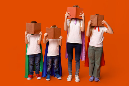 Cute kids dressed as superhero covering faces books on orange background. Library Lovers Dayの写真素材