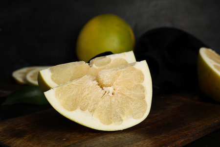 Wooden board with pieces of fresh pomelo fruit on black background