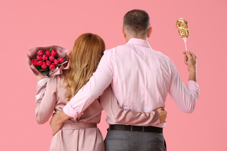 Middle-aged couple with bouquet and balloon in shape of figure 8 on pink background. International Women's Dayの写真素材