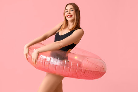Beautiful young woman in tank swimsuit and with inflatable ring on pink backgroundの写真素材