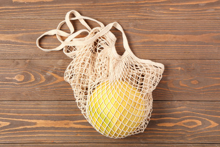 Fresh juicy pomelo in string bag on wooden table
