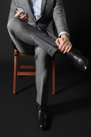 Young man in elegant shoes sitting on chair against black backgroundの写真素材